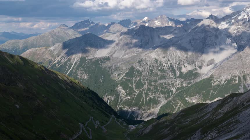 Rolling clouds create shadows on mountain range peaks in the Alps