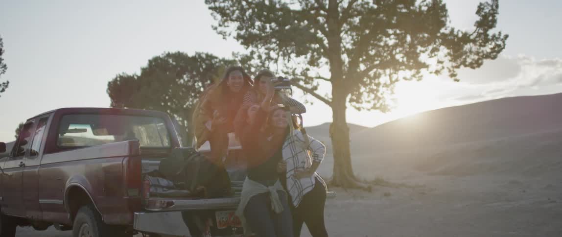 Female friends pose for a photo as they unload a pickup truck