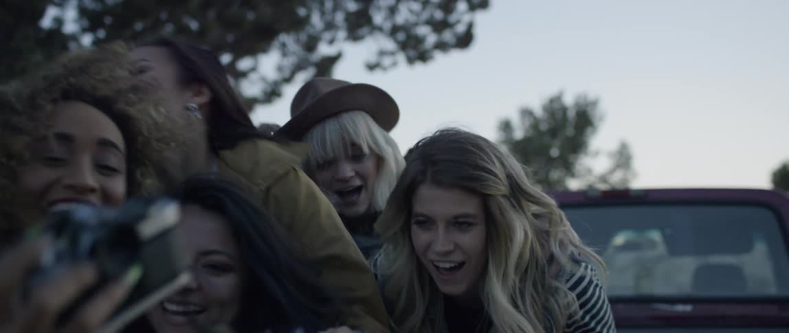 A group of women pose for a camera outside on a windy day
