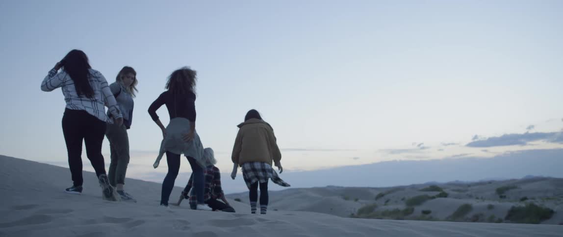 Group of women walk outside on sandy hills at sunset