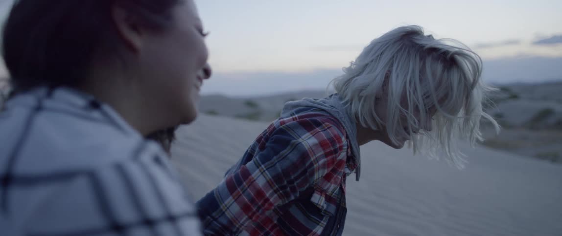 Two women sit in the sand and laugh
