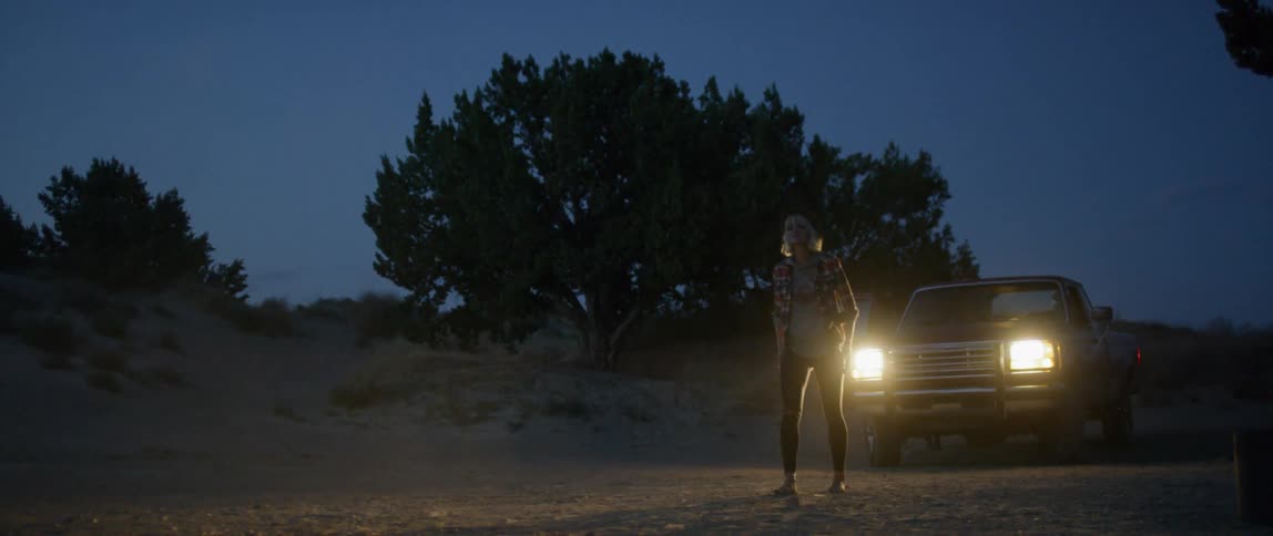 Person walks in front of a vehicle with shining headlights outside at night