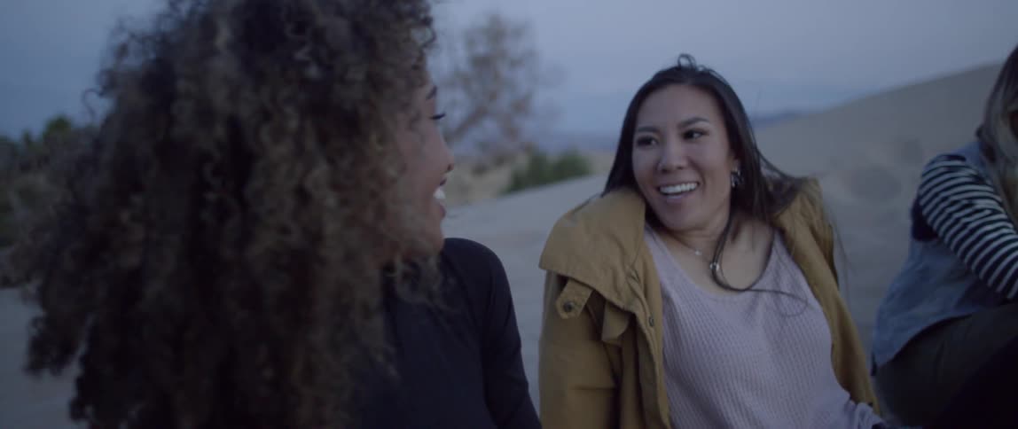Three women laugh and talk outside in the desert