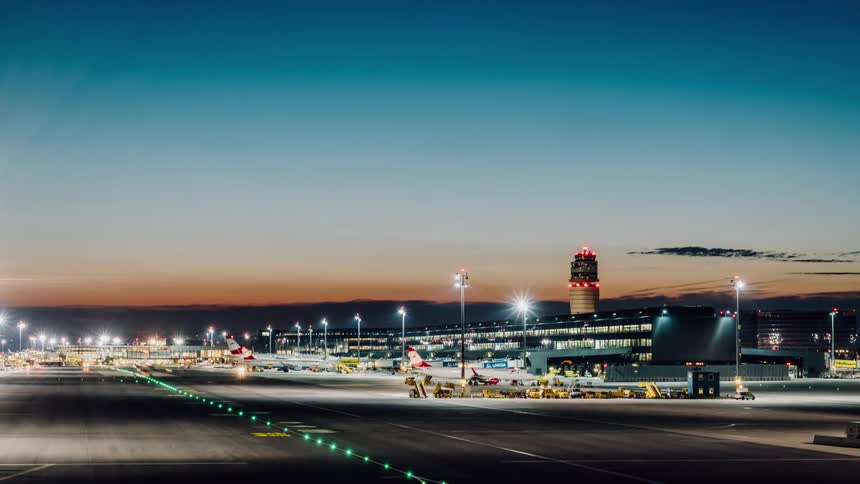 Airplanes and workers travel on a busy tarmac at an airport at dusk