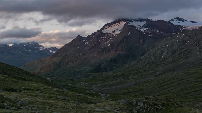 Storm clouds are moving across a mountain range at dusk