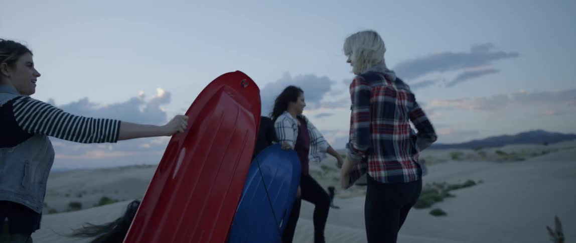 A group of women stand atop a sand hill with sleds