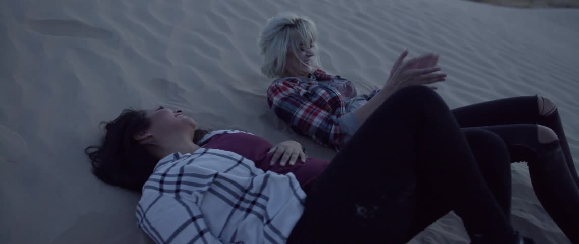 Girlfriends lay back against the sand and laugh together