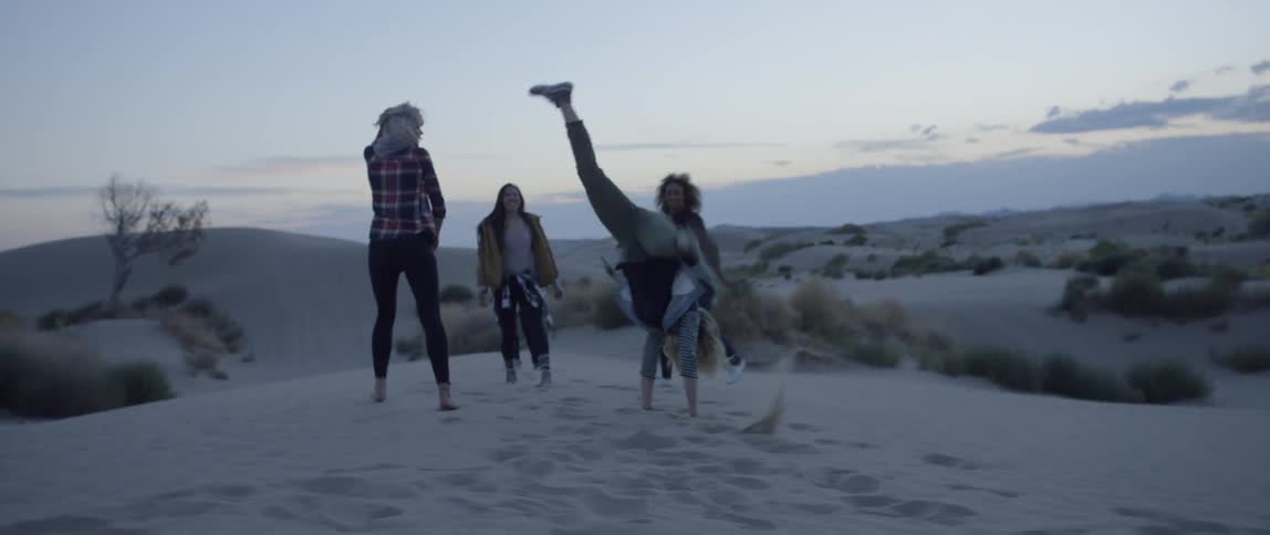 A group of friends walk and cartwheel in a desert at sunset