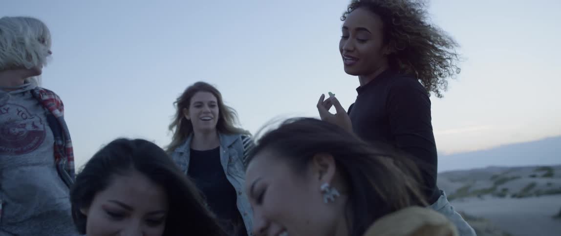 Group of women smile and laugh looking at a phone outside in the evening