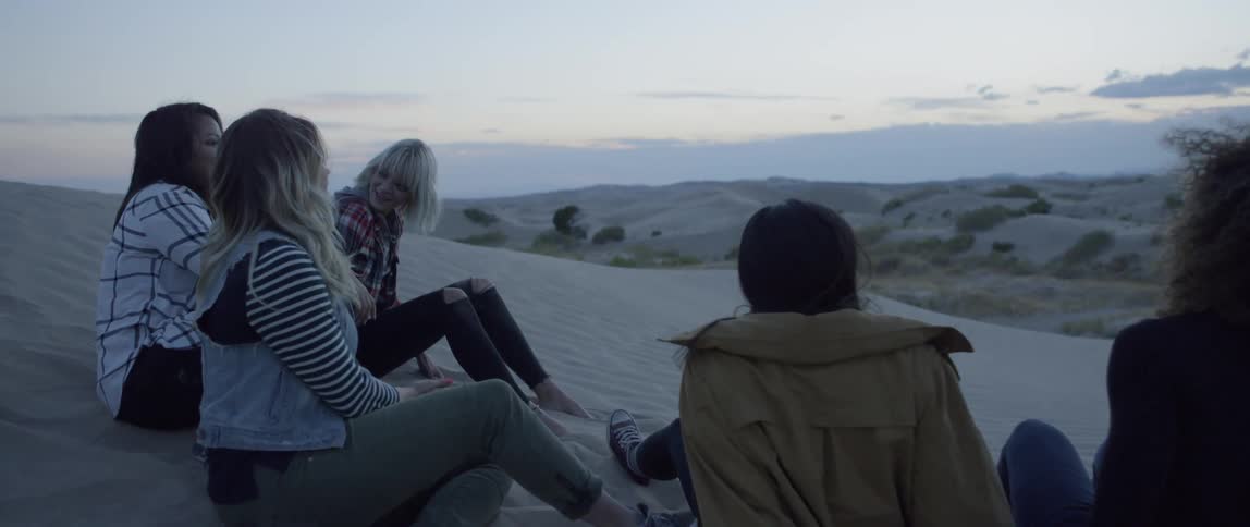A group of women sit on a sand hill and talk