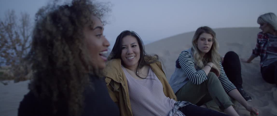 A group of women sit on a sand hill and talk