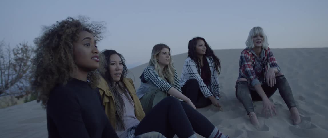 A group of women sit on a sand hill and talk
