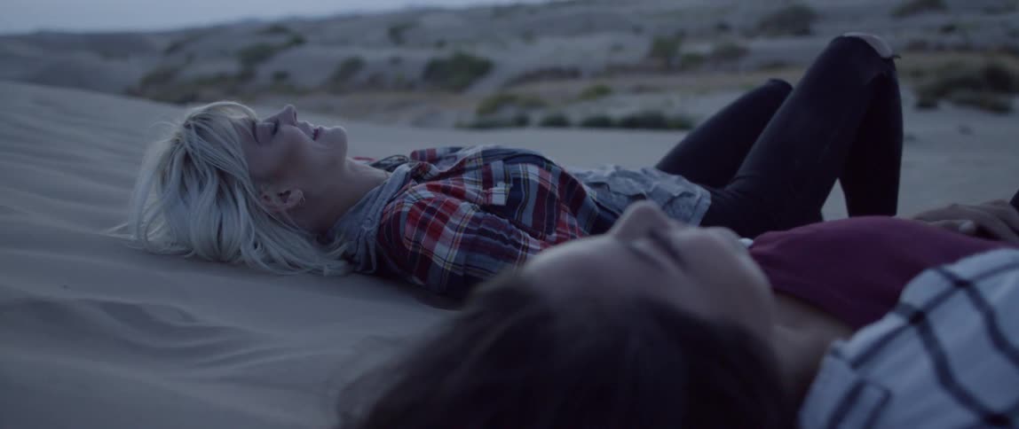 Two women lay outside in the sand at night