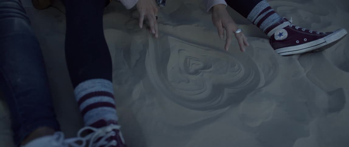 A woman draws a heart in the sand with her fingers