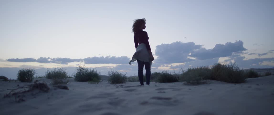 A woman stands in the sand as the breeze blows her shirt around her waist