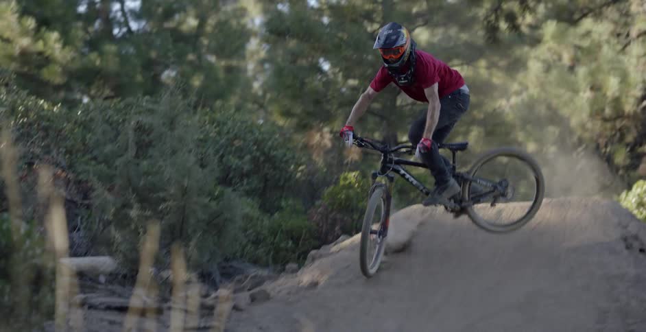 A bicyclist jumps over a dirt ramp in a forest