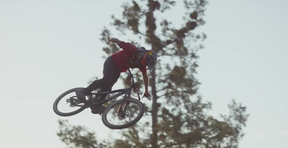 A bicyclist jumps over a dirt ramp and spins in the air
