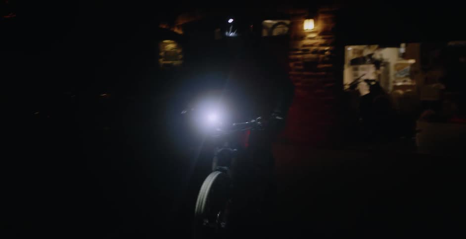 Person gets on a bike outside of their garage and rides away at night