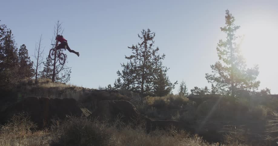 A man does a jump over a hill on a sunny day