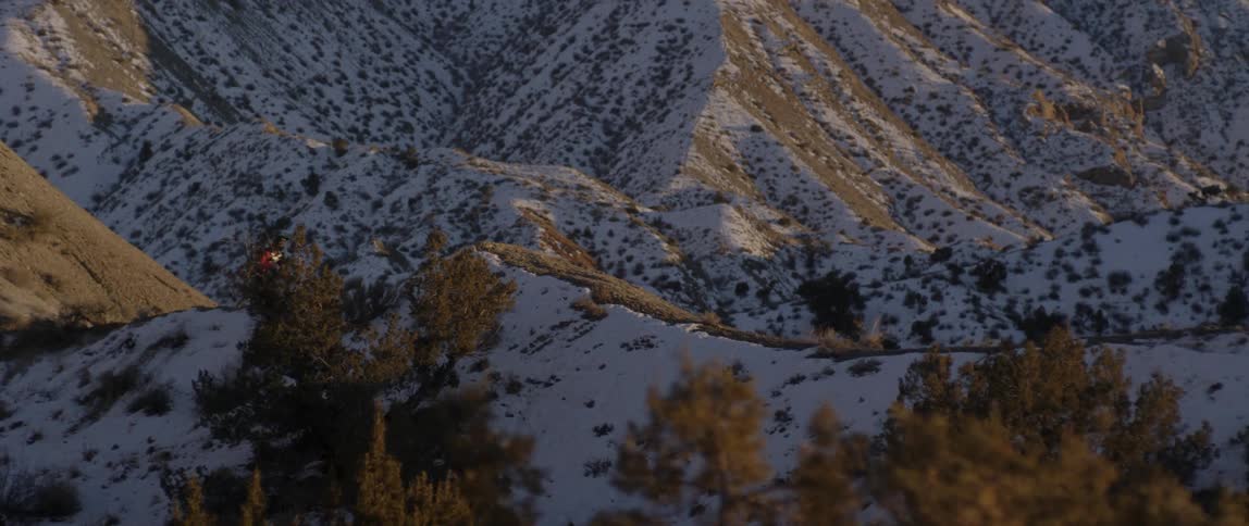A bicyclist jumps and does a trick in snowy mountains at sunset