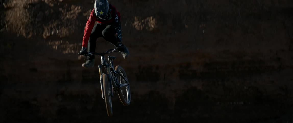 A bicyclist jumps off a dirt ramp and performs a trick