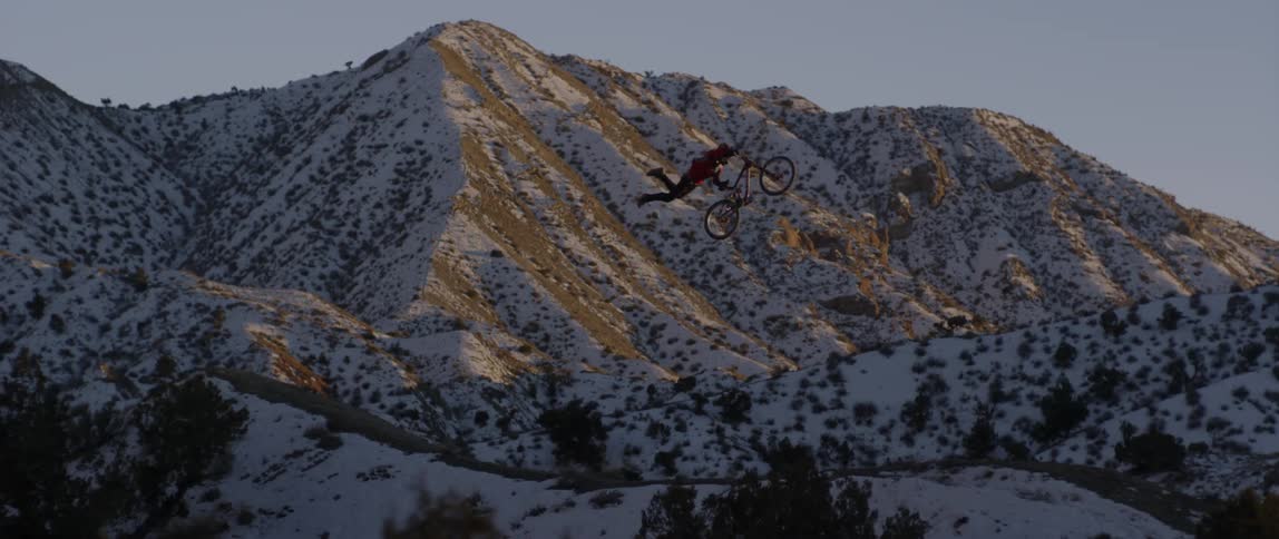 A bicyclist jumps and does a trick in snowy mountains at sunset