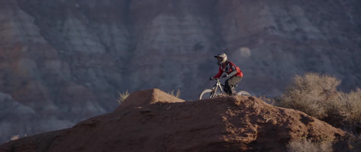 A person bikes down and off a hill with a twist