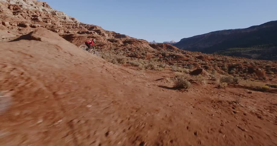 A mountain bike rider does a flip off an embankment in the desert during the day