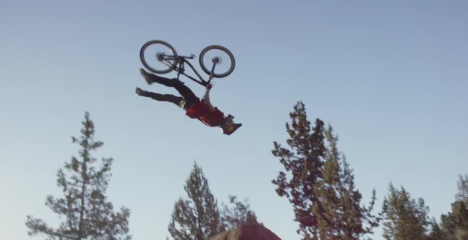 A rider on a mountain bike jumps off a ramp and flips