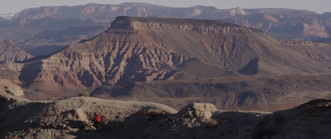 A drone flies next to a bicyclist doing tricks in mountains