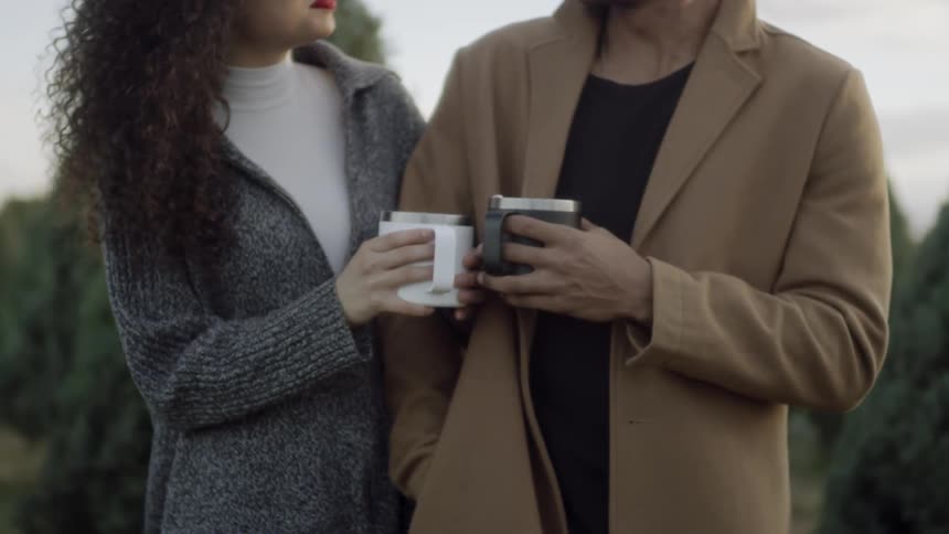 A woman and man are standing outside with cups of a warm liquid