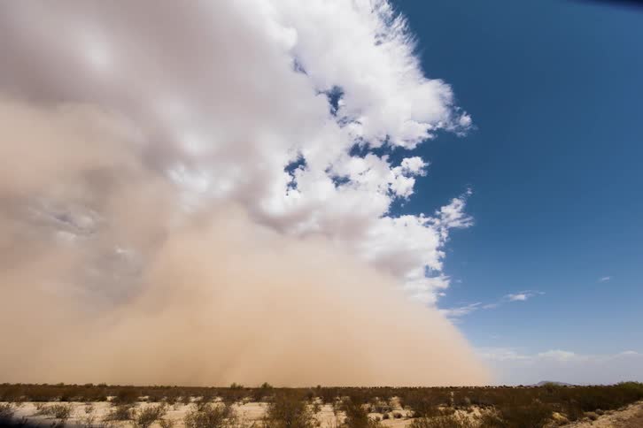 A sand storm is moving across the desert in daylight