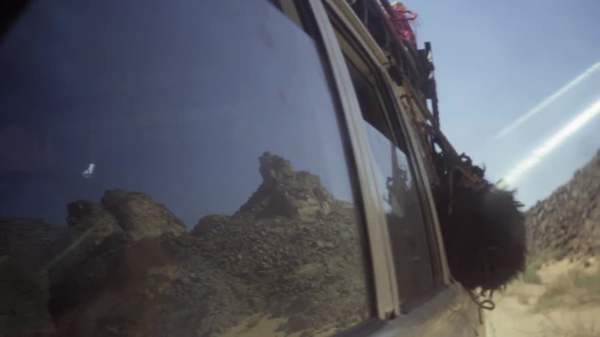A dog is hanging its head out of the window of a vehicle traveling on a desert road