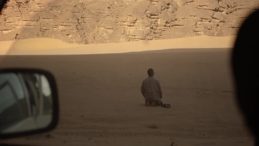 A man is kneeling down to pray in the desert during the day