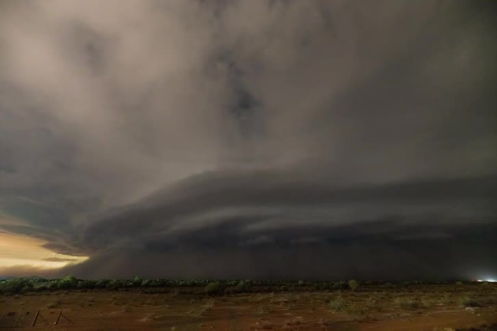 A dust storm with lightning is moving across a desert landscape at dusk