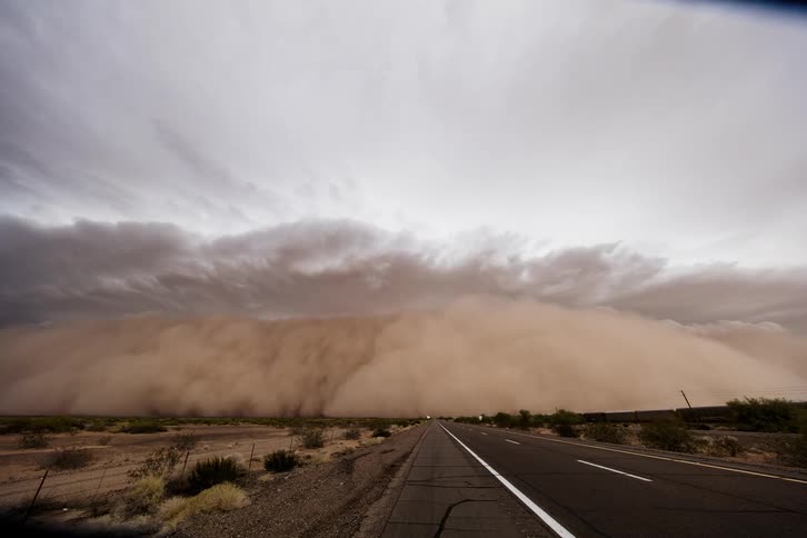 A sand storm is moving across a desert highway at dusk