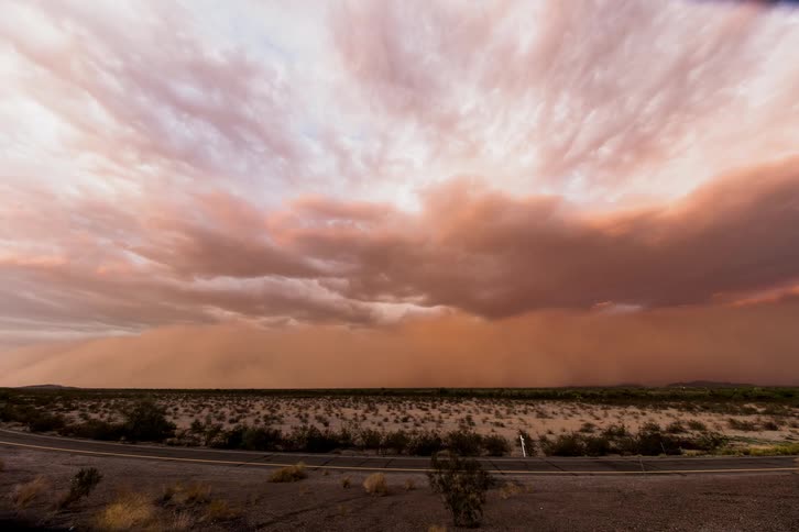 A sand storm is moving across the desert in daylight