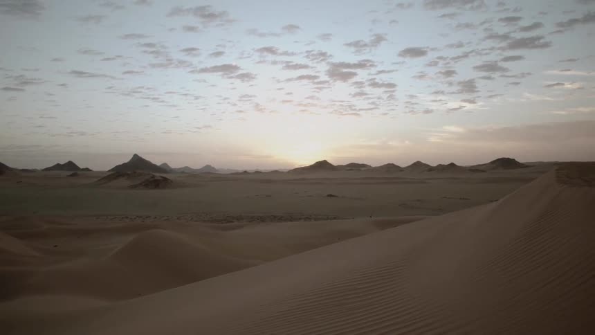 Clouds dot the sky over peaks and sand dunes at sunset