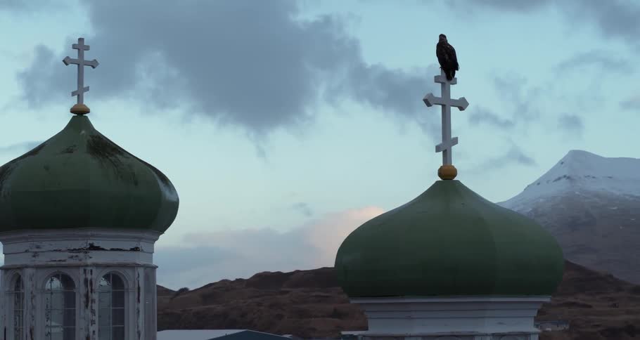 An eagle is perching on a church cross at dusk