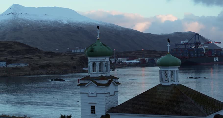 Birds are perched on the crosses of a church near the mountains and ocean