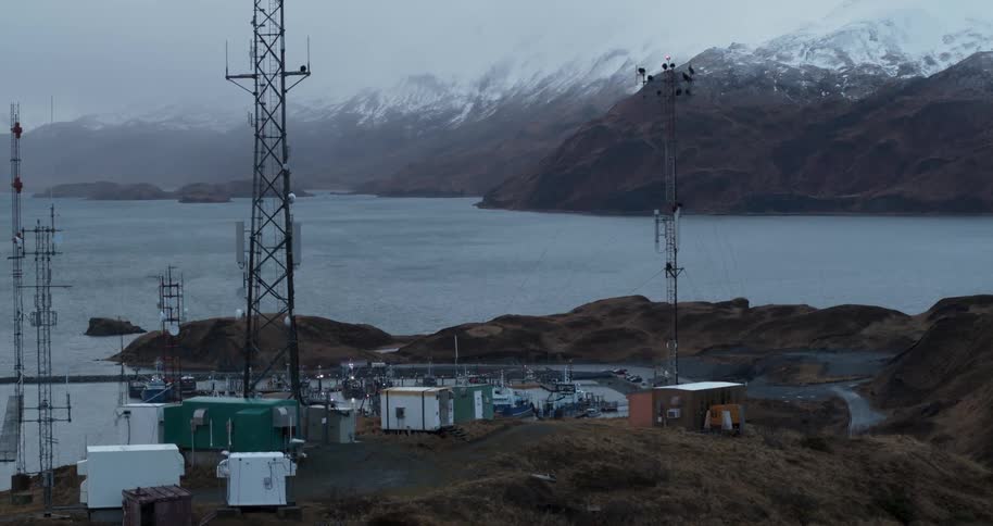 A radio tower sits on top of a large hill overlooking a small town and ocean