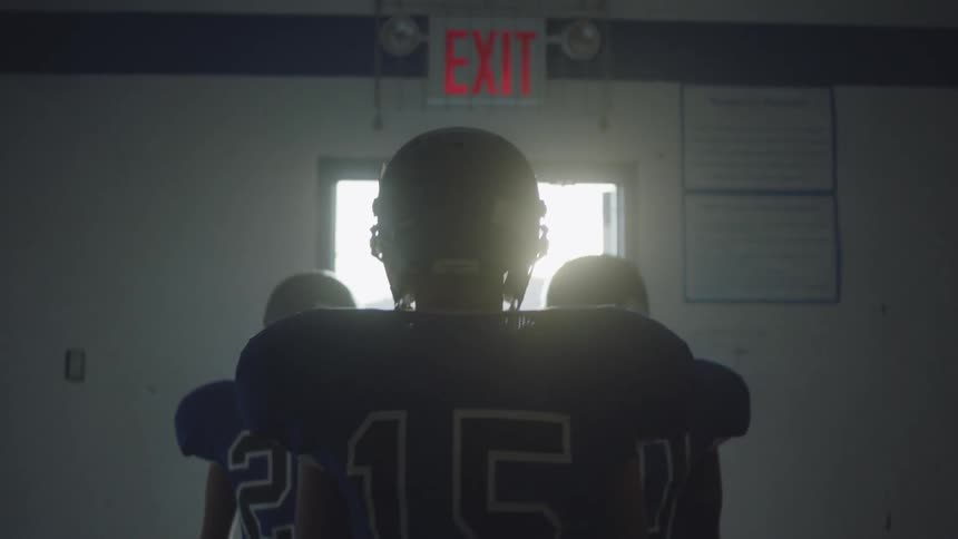 Football players walk towards a lit doorway