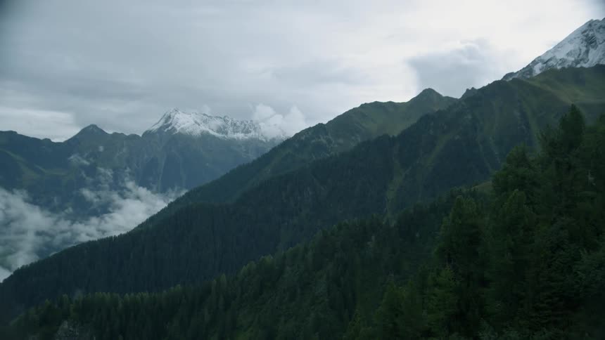 Clouds are lingering amid the hillsides of a mountain range in winter
