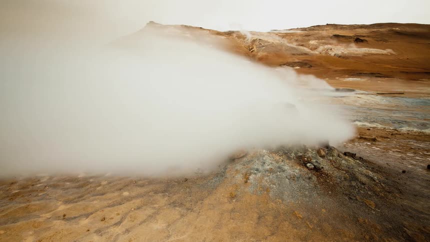 Steam is rising from hot springs in a natural landscape on a windy day
