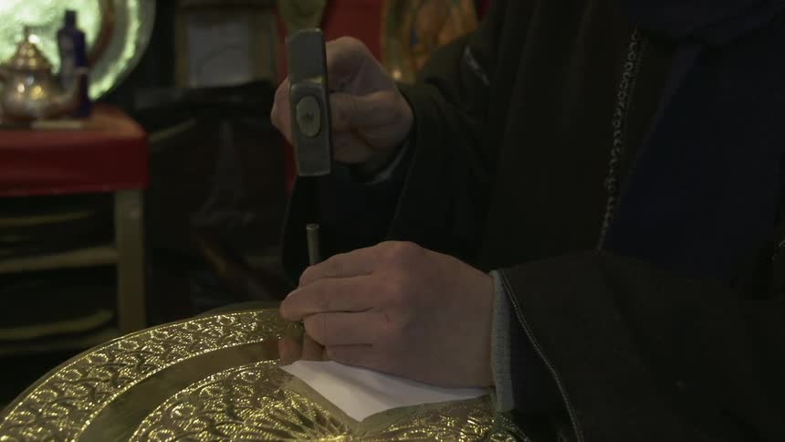 Man uses a chisel and hammer to decorate a gold platter