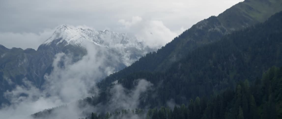 Clouds are lingering amid the hillsides of a mountain range in winter