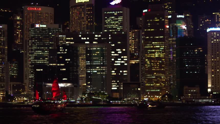 A boat floats in front of skyscrapers at night