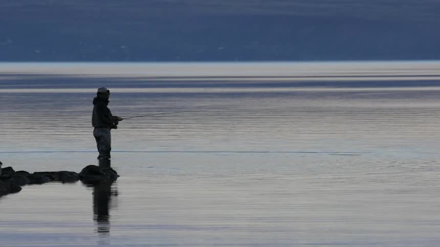 A man fishes in a lake at sunset