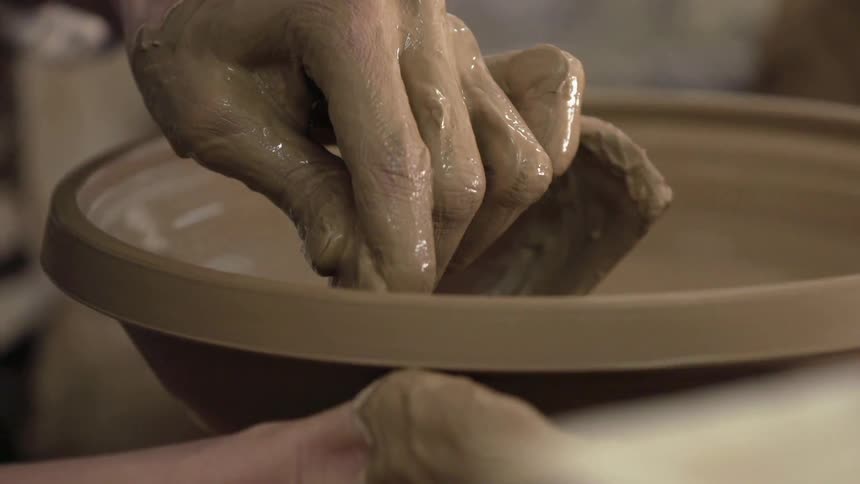 Hands shape a bowl on a pottery wheel