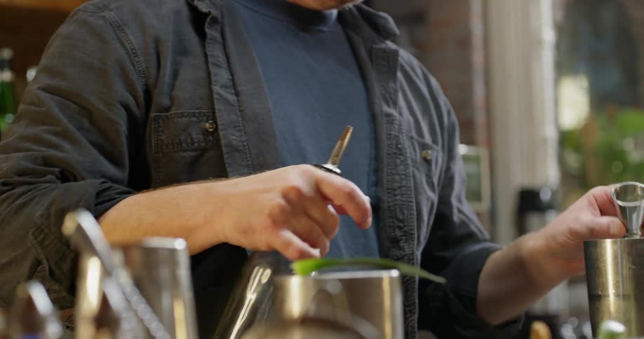 A bartender is pouring liquid into a shaker to make a mixed drink